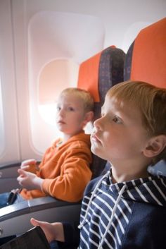 two young boys sitting on an airplane seat looking out the window at something in the distance