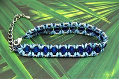 a blue beaded bracelet with silver beads on a leafy green background, the clasp is made out of glass beads