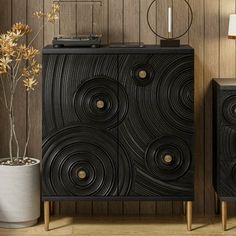 a black cabinet sitting next to a plant in a vase on top of a wooden floor