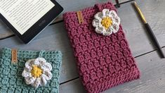 two crocheted pouches sitting on top of a wooden table next to an electronic device