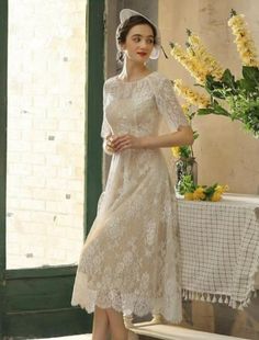 a woman in a dress and hat standing next to a table with flowers on it