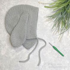 a crocheted hat next to a knitting needle and green needles on a white surface