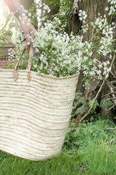 a person holding a basket full of flowers in the grass next to a tree and fence