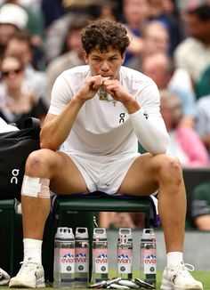 a tennis player sitting on the sidelines with his hand in his mouth and several empty water bottles next to him