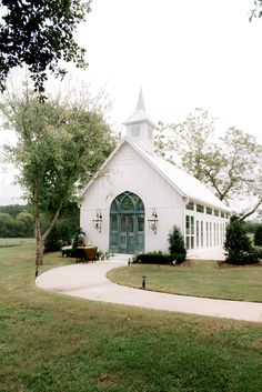 a white church with a blue door and steeple on the front is surrounded by green grass