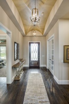 an empty hallway with a chandelier hanging from the ceiling and wood flooring