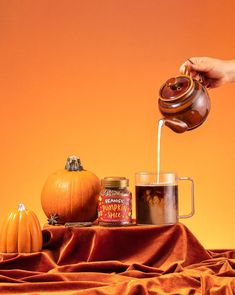 a person pouring tea into a cup on top of a table covered in pumpkins