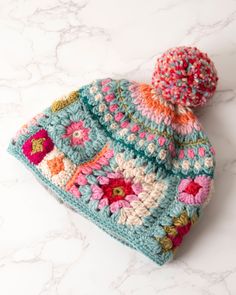 a crocheted hat with a pom - pom sits on a marble surface