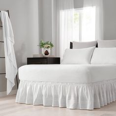 a white bed with ruffled bedspread and pillows