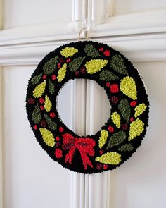 a crocheted christmas wreath hanging on the front door with red, green and yellow decorations