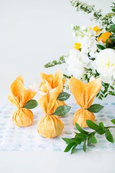 three small yellow flowers sitting on top of a table next to white and yellow flowers