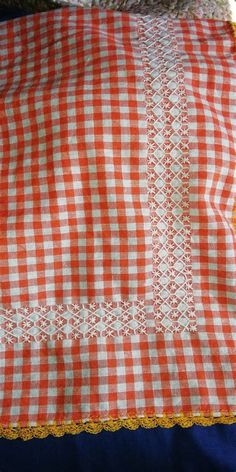 an orange and white checkered table cloth with yellow lace trim on the edge, sitting on a blue surface