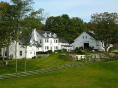 a large white house sitting on the side of a lush green field next to a forest