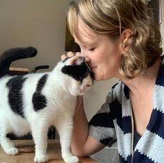 a woman kissing a black and white cat on top of a wooden table in front of a mirror