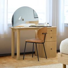 a desk with a mirror and chair next to it in front of a window on a wooden floor