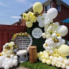 balloons and sunflowers are on display in front of a lawn with a white wicker chair