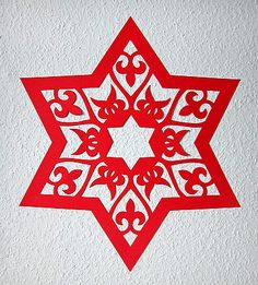 a red paper cut out of a star on a white wall with an intricate design