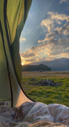 the sun is setting over an open field with a tent and mountains in the distance