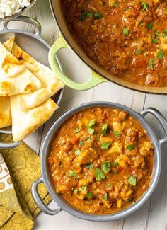 two pans filled with food next to rice and pita bread