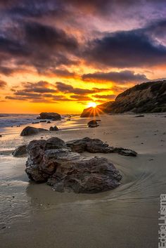 the sun is setting over some rocks on the beach