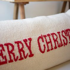 a red merry christmas pillow sitting on top of a wooden table next to a chair