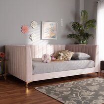 a pink daybed with pillows on it in front of a gray wall and wooden floor