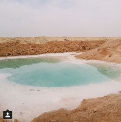 a large pool of water surrounded by dirt and sand in the middle of an arid area