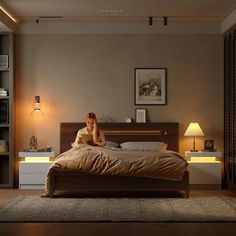 a woman sitting on top of a bed next to a night stand and lamp in a bedroom