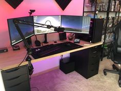 a computer desk with two monitors and a keyboard on it in front of a pink wall