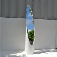 a large white mirror sitting on the side of a wall next to a tree and building