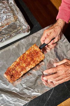 a person is cutting some food on a piece of tin foil with a black knife