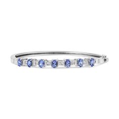 Wrap your wrist in the prettiest shade of blue. Our 14K White Gold bangle bracelet showcases 7 oval tanzanite stones measuring in at a whooping 5MM each. Diamond-accented sections highlight each lovely violet stone. The bangle has 24 natural, baguette diamonds for a total weight of 1/4 carats. Each diamond channel set and is approximately H-I in color and VS2-SI1 in clarity. A box clasp and hinge will secure this treasure to your wrist. Blue Oval Diamond Bracelet With Jewels, Timeless Blue Round Bracelets, Blue Diamond Bangle Fine Jewelry Bracelet, Blue Diamond Bangle Bracelet Fine Jewelry, Blue Diamond Bangle Bracelet In Fine Jewelry Style, Blue Diamond Bangle Bracelet With Accents, Oval Sapphire Bracelet In White Gold, Oval Sapphire Bracelets In White Gold, Blue Oval Sapphire Diamond Bracelet