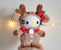 a hand holding a hello kitty crochet stuffed animal with lights in the background