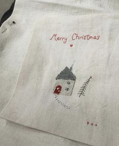 a white linen bag with a house and christmas tree embroidered on the front, sitting on top of a table