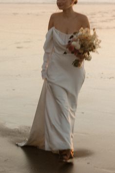 a woman in a white dress is walking on the beach