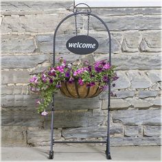 a welcome sign hanging from a metal frame with flowers in front of a stone wall