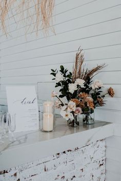 a table topped with flowers and candles on top of a white counter next to a wall