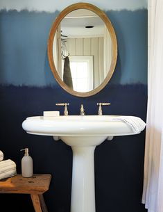 a white pedestal sink sitting under a mirror in a bathroom next to a wooden stool