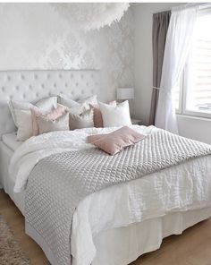 a bed with white sheets and pink pillows in a bedroom next to a large window