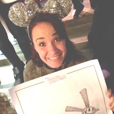 a woman holding up a drawing in front of her face and smiling at the camera