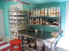 a kitchen filled with lots of bottles and pans on top of metal shelves next to a red stool