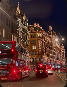 two double decker buses driving down the street in front of buildings with christmas lights on them