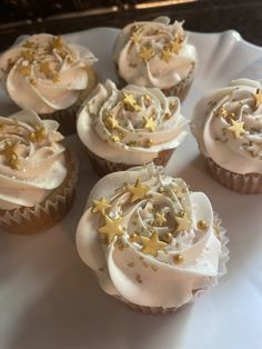 several cupcakes with white frosting and gold stars on them sitting on a plate