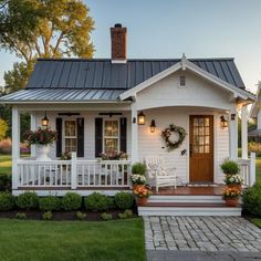 a small white house with flowers and wreaths on the front porch is lit up at night