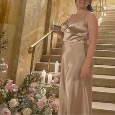 a woman in a long dress holding a drink standing on some stairs with flowers and candles