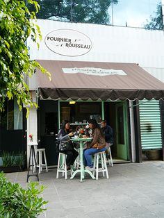 three people sitting at a table in front of a building with an awning over it