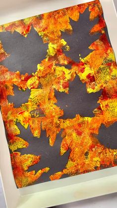 an orange and yellow painting is on a white plate with a black background that looks like autumn leaves