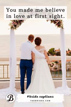 a bride and groom looking at the ocean from their wedding ceremony venue in front of an arch decorated with flowers