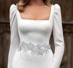 a woman wearing a white dress with long sleeves and an embellished belt on her waist