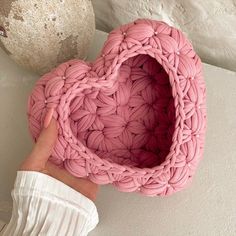 a pink heart shaped basket sitting on top of a white wall next to a stone ball